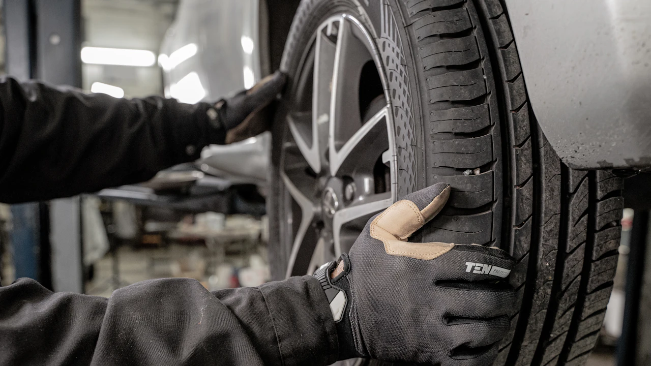 A technician in gloves working on a car wheel and tyre in a workshop