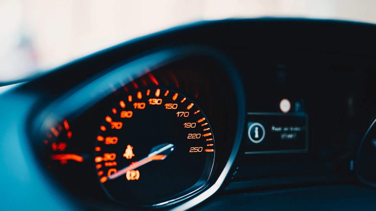 A car's instrument cluster in daylight: an orange-lit speedometer, warning lights and a message display beside it.