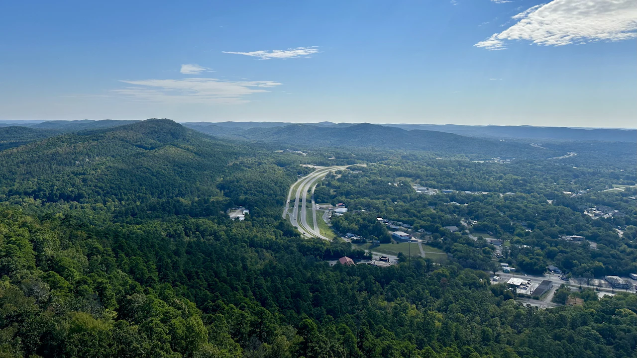 An elevated view of a highway winding through dense green Arkansas forest under a clear sky