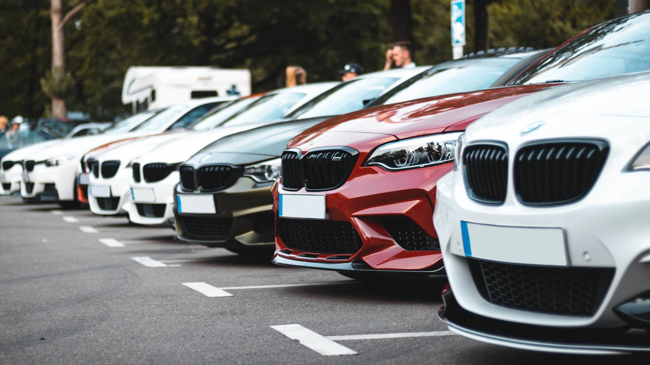 A row of cars parked front-on in a lot, bonnets and grilles receding into the distance