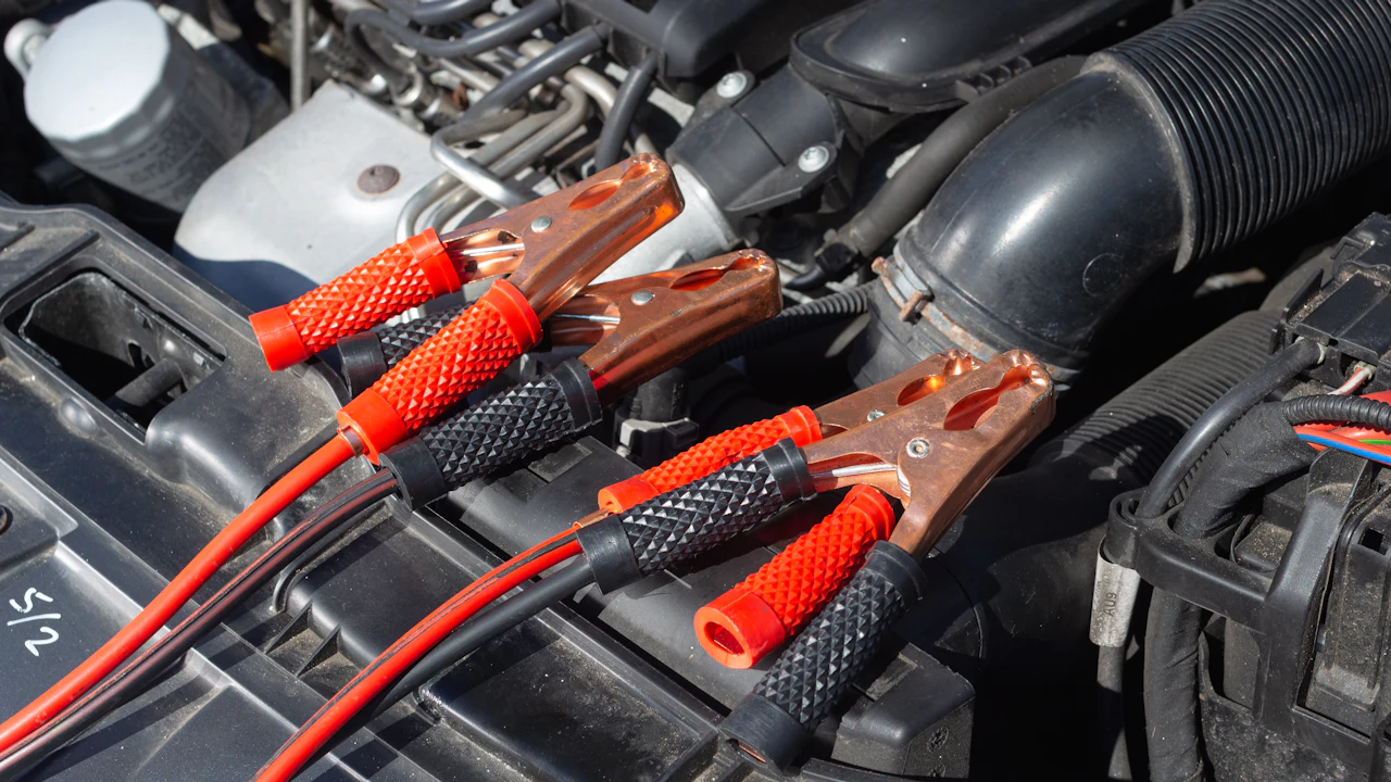 Jump leads clamped onto terminals in an engine bay, red and black cables running out of frame