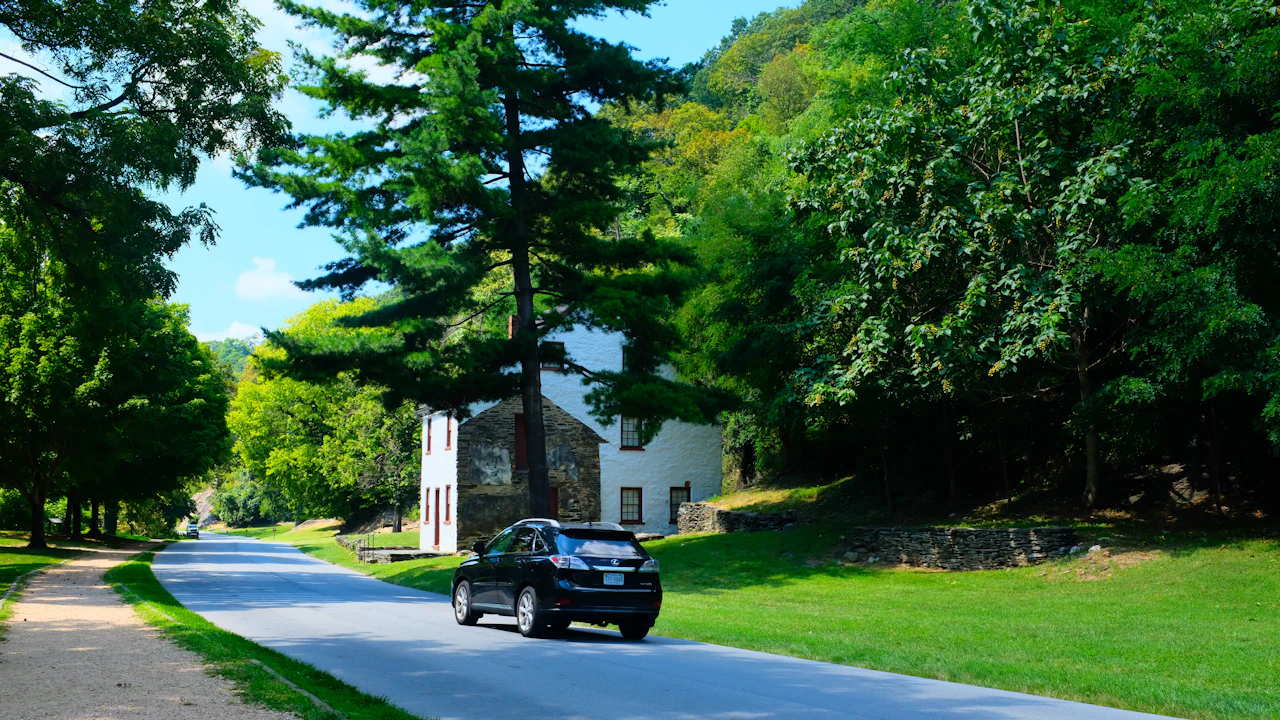 A dark SUV on a tree-lined Virginia parkway past a stone and white-painted historic building