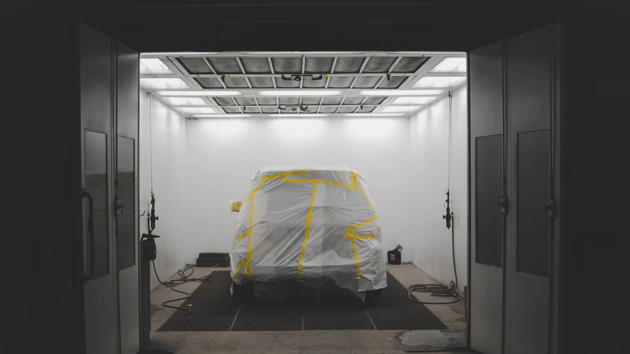 A car part-masked with tape and paper in a workshop, ready for a panel to be refinished