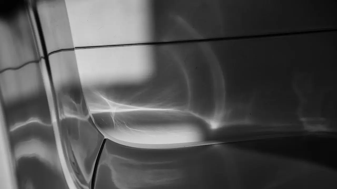 Black-and-white close view of a car's front wing and bumper corner, light catching a dent in the panel.