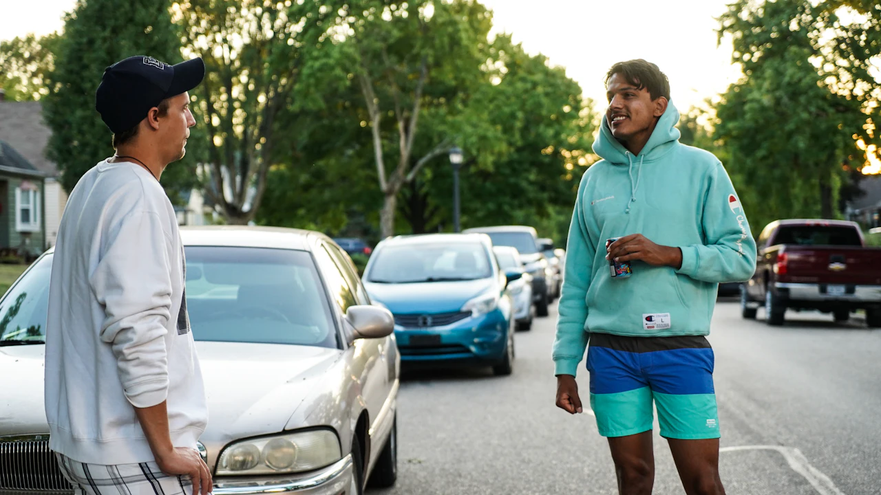 Two people standing beside a car outdoors, talking, one gesturing toward the vehicle