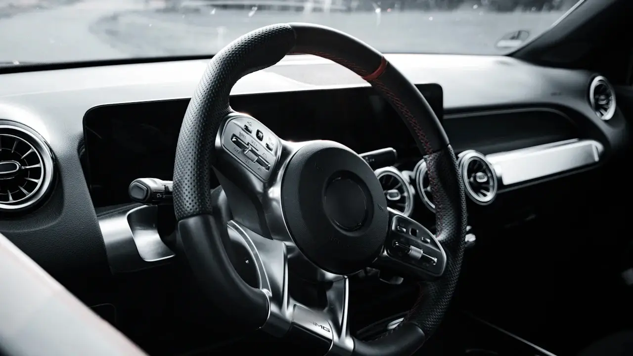 A modern car cabin in black and white: steering wheel, screens and round air vents; wheel emblems blurred.