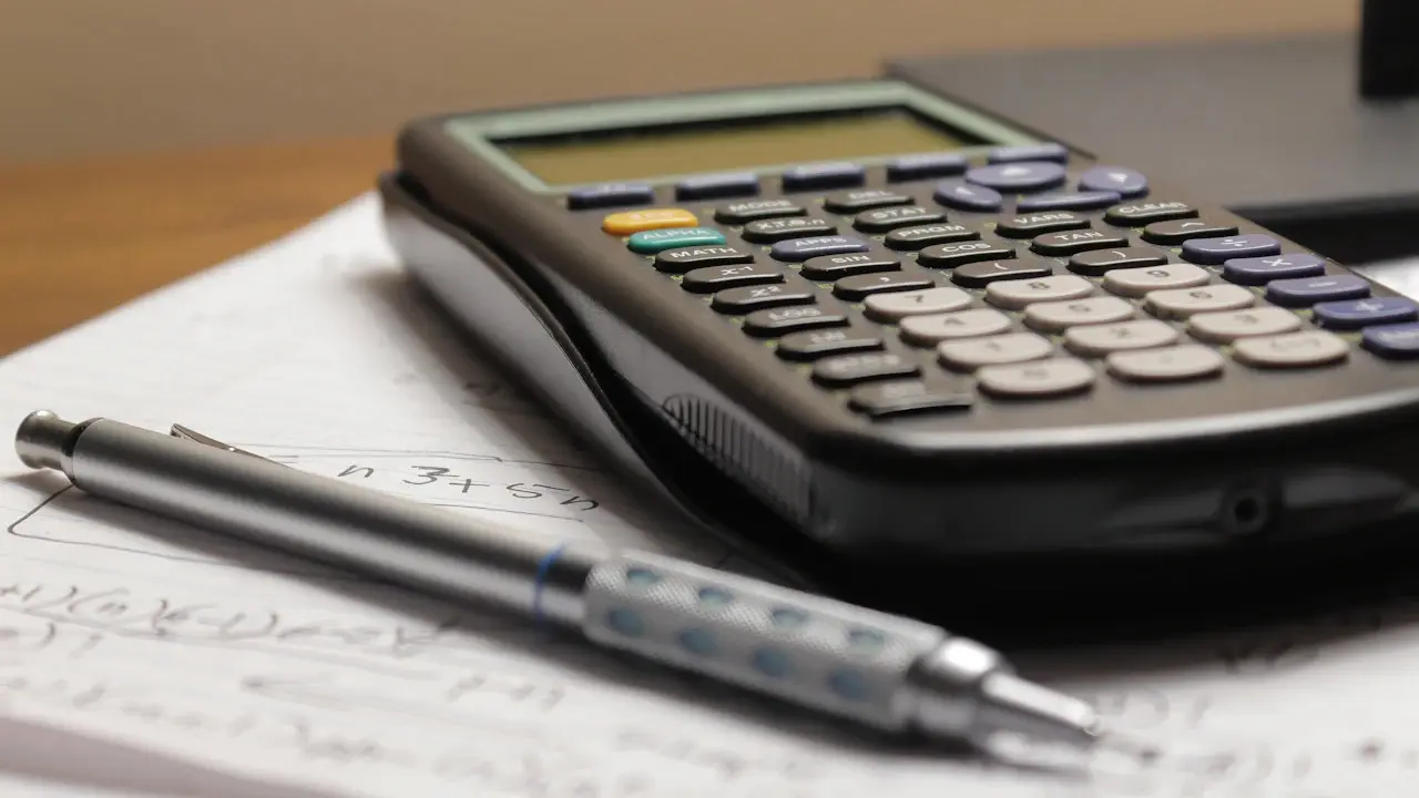 A calculator and a pen lying on a page of handwritten sums.