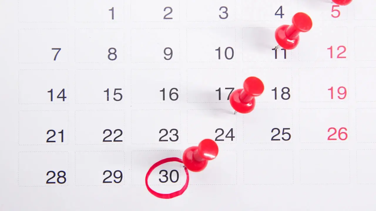A wall calendar with red pins in three dates and the 30th circled in red.