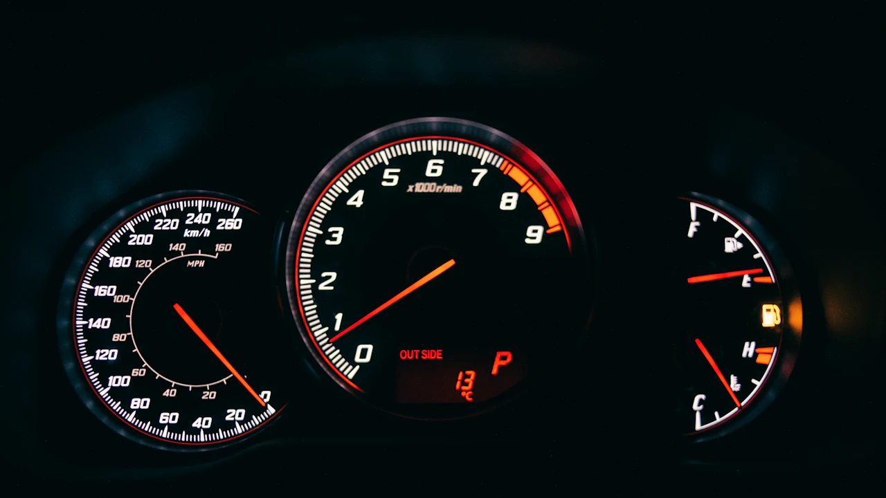A car's instrument cluster lit at night: speedometer, tachometer, fuel and temperature gauges, with an amber warning light on.