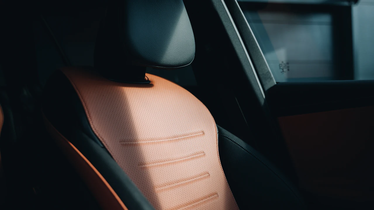 A tan leather car seat photographed from the side, stitching and bolster in view