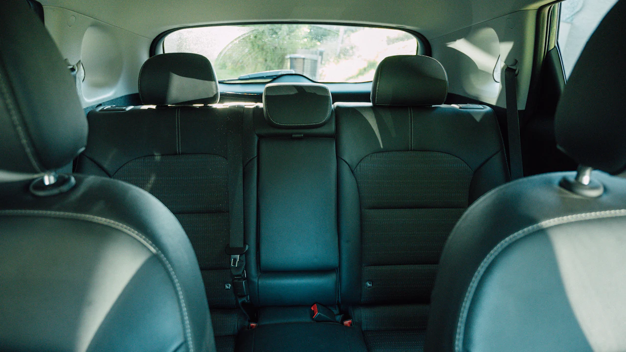 The rear bench of a hatchback seen between the front seats, with fabric-and-leather upholstery, three head restraints, seat-belt buckles and the rear window and wiper.