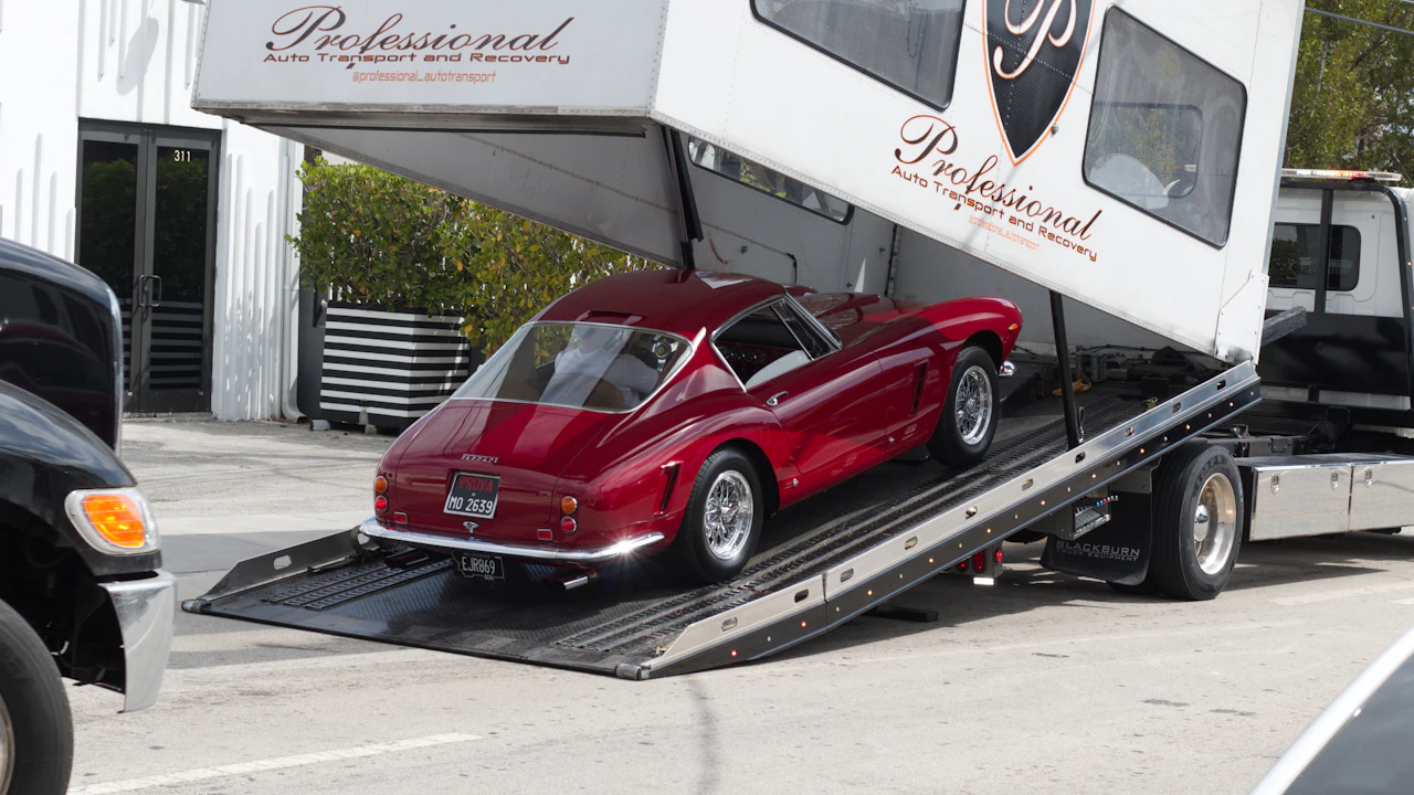 A dark red classic coupe being loaded up the ramps of a flatbed vehicle transporter outside a recovery company&rsquo;s unit