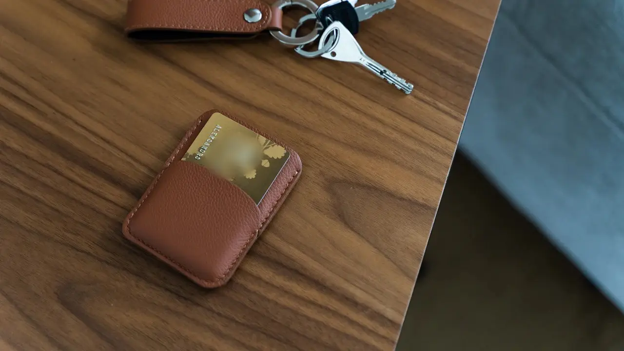 A set of keys and a bank card in a leather holder on a wooden table.