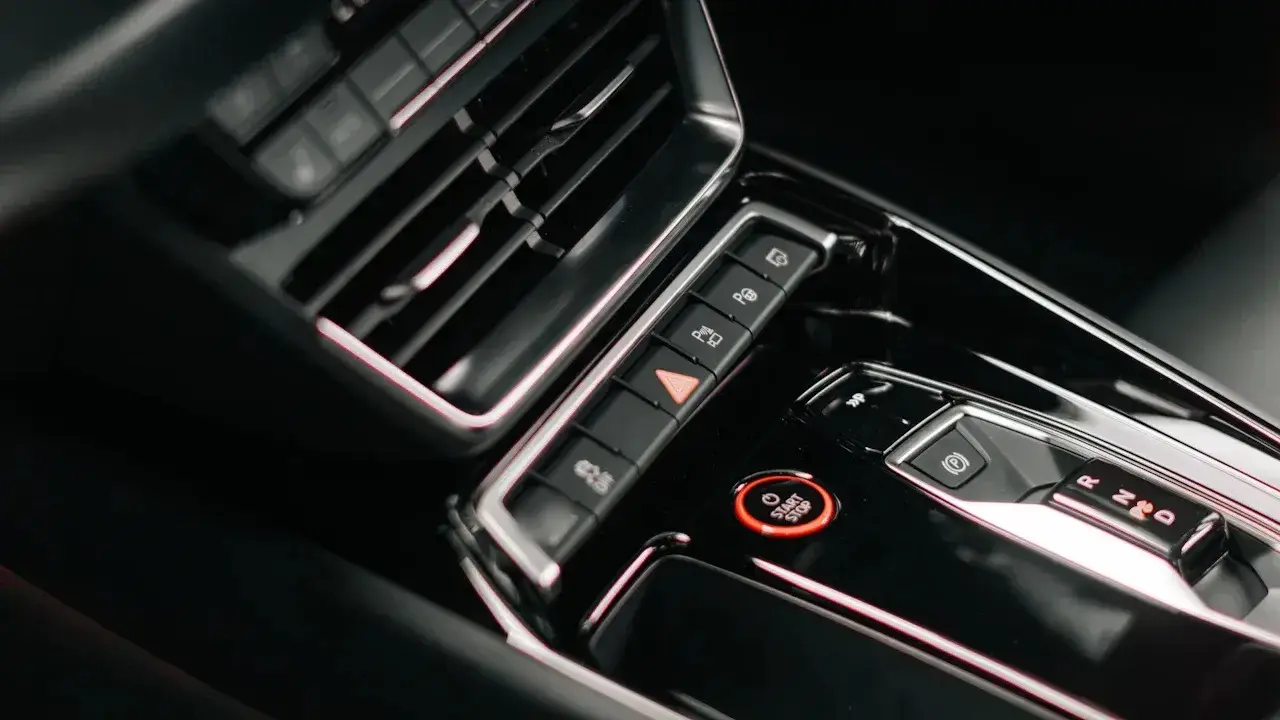A car's centre console: a red start-stop button, the hazard and parking switches, the gear selector and an air vent.