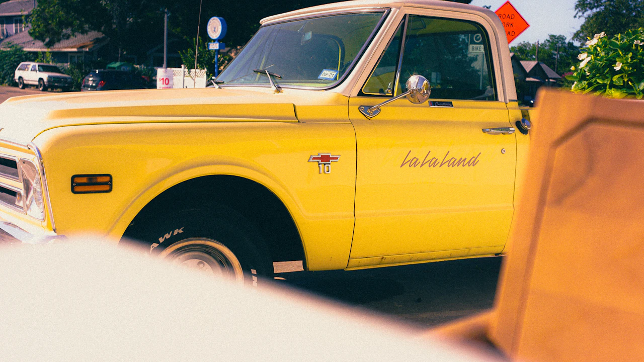 A yellow classic Chevrolet pickup truck parked at the kerb, side view showing the cab and chrome wing mirror