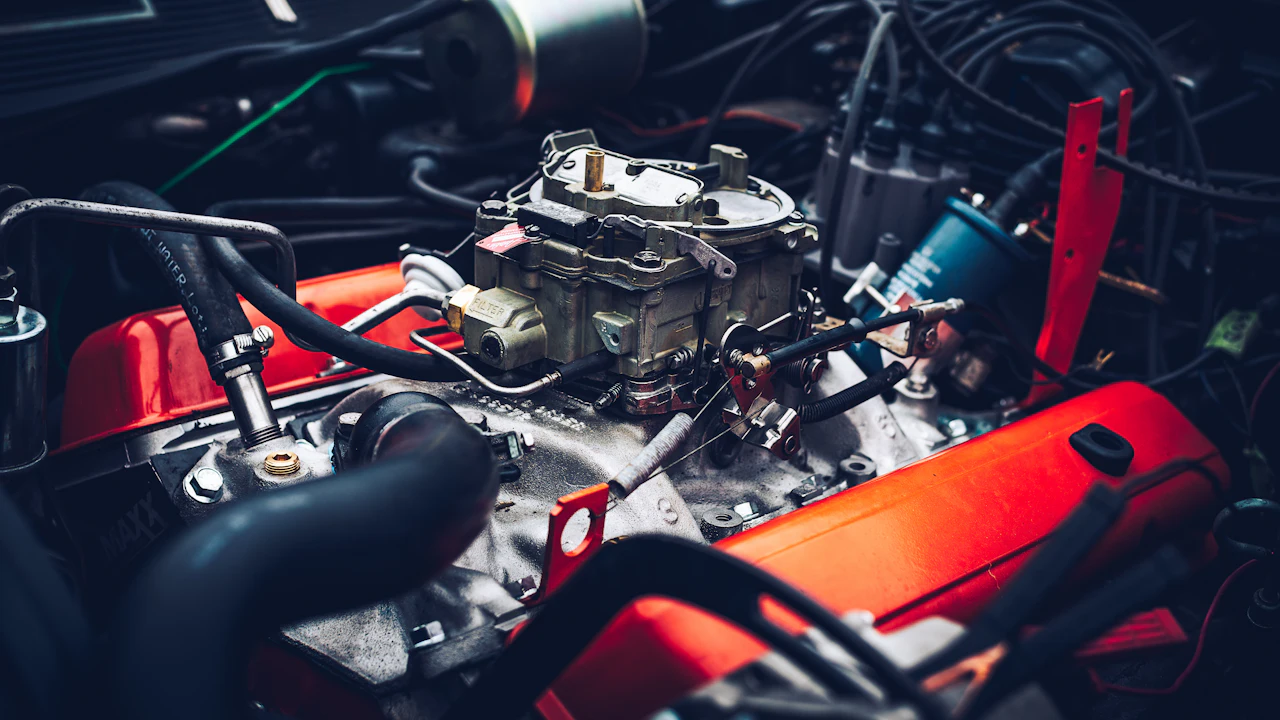 A carburetted V8 engine bay with orange valve covers, a four-barrel carburettor on the intake manifold and distributor leads running across the engine