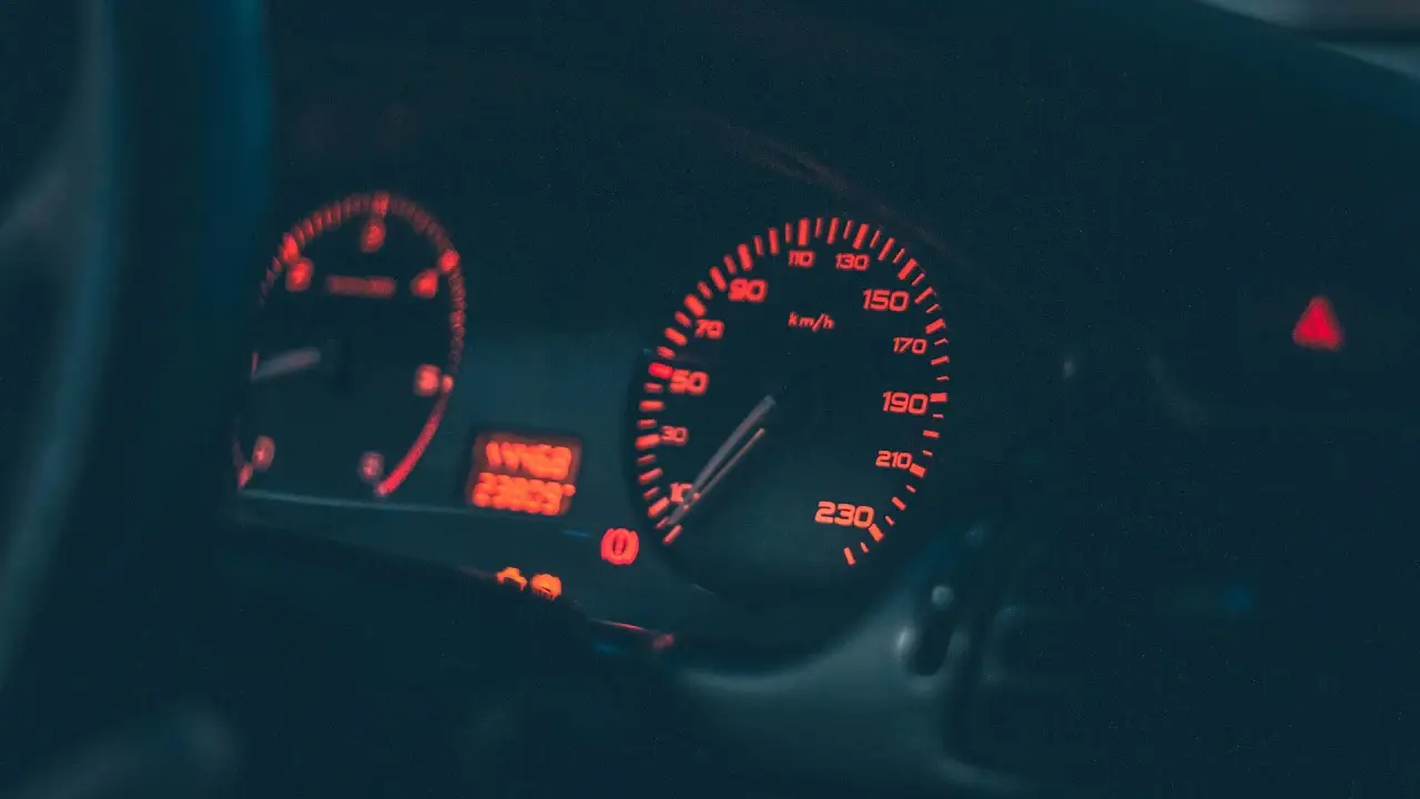 A car’s instrument cluster lit red at night, with warning lamps on.