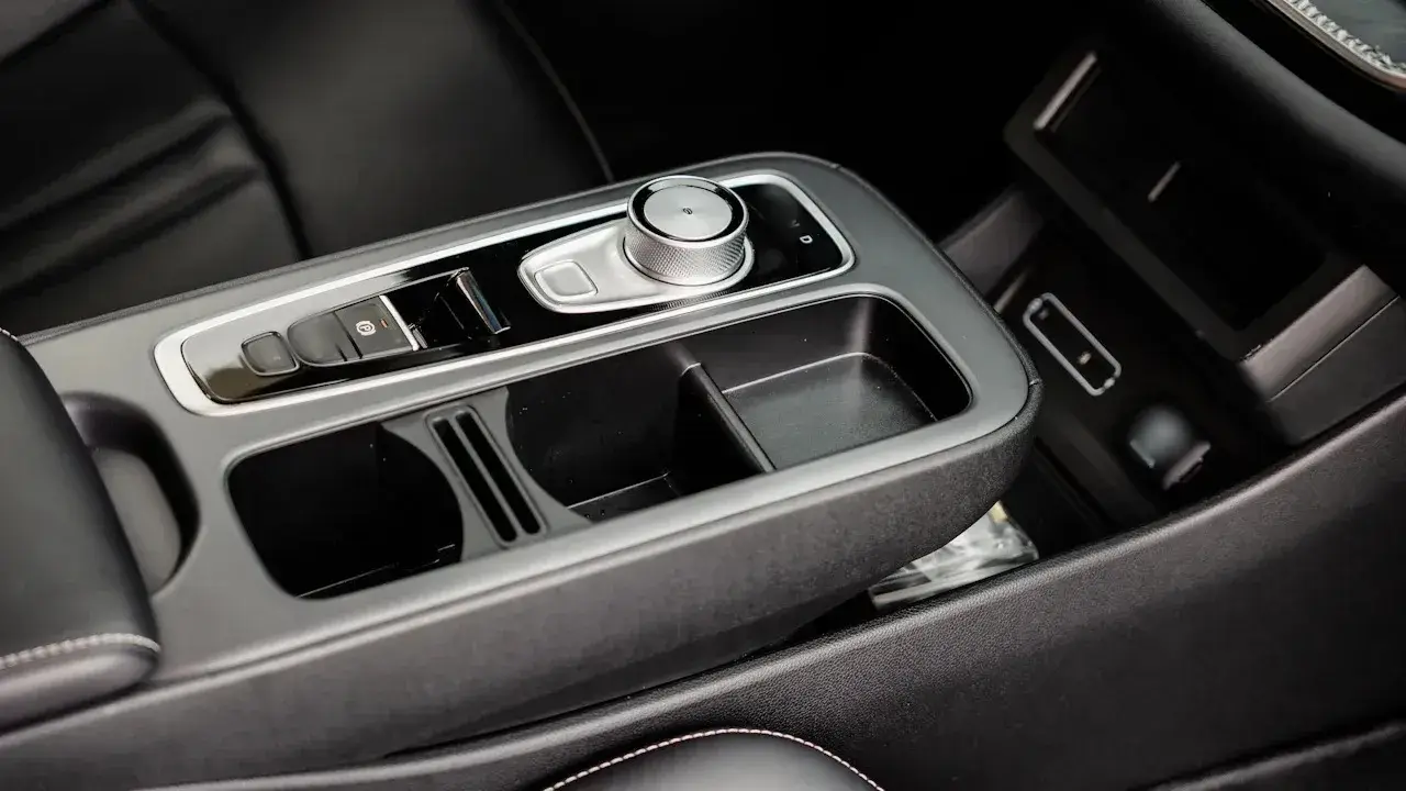 A car's centre console with a gear dial, an open storage bin and a phone tray beside the dashboard.
