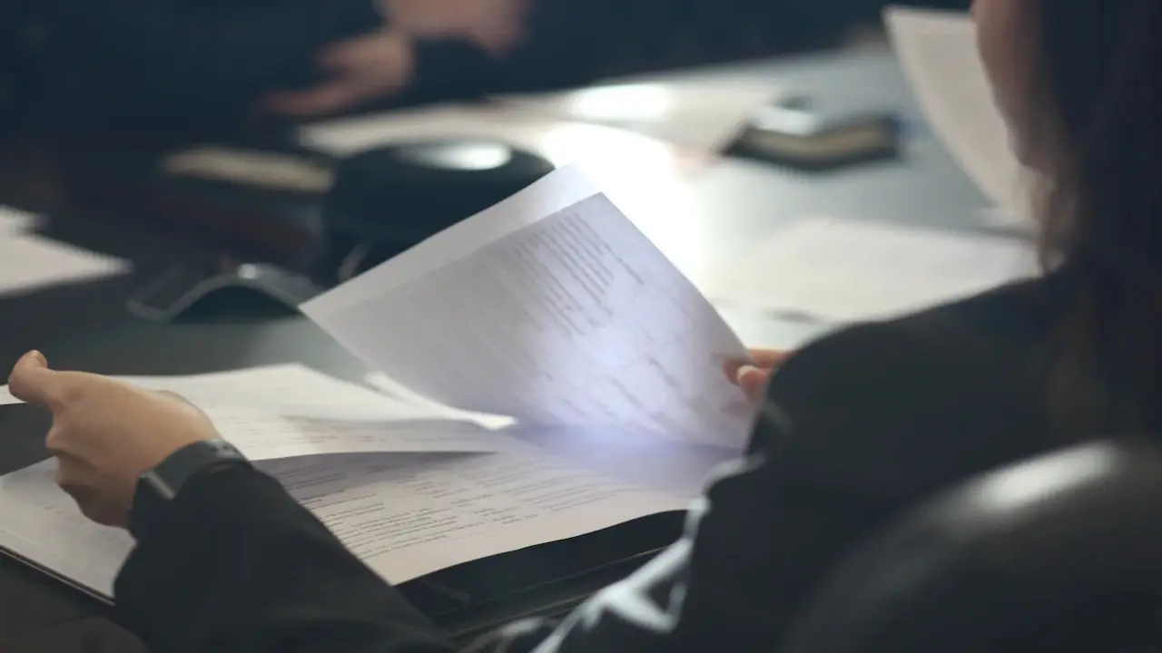 A person reading a printed multi-page agreement at a table.