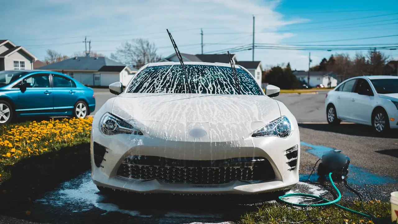 A white coupe covered in wash foam, seen from the front.
