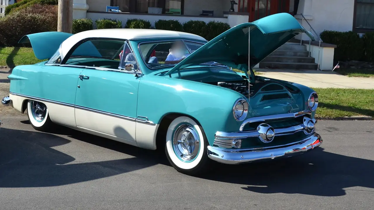 A vintage two-tone coupe parked on a street with its hood open.