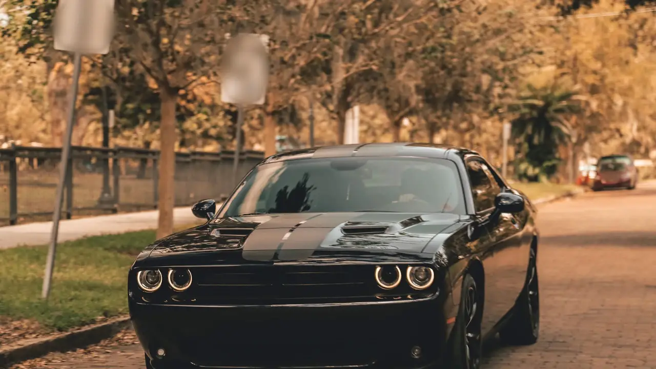 A black coupe parked on a tree-lined street.