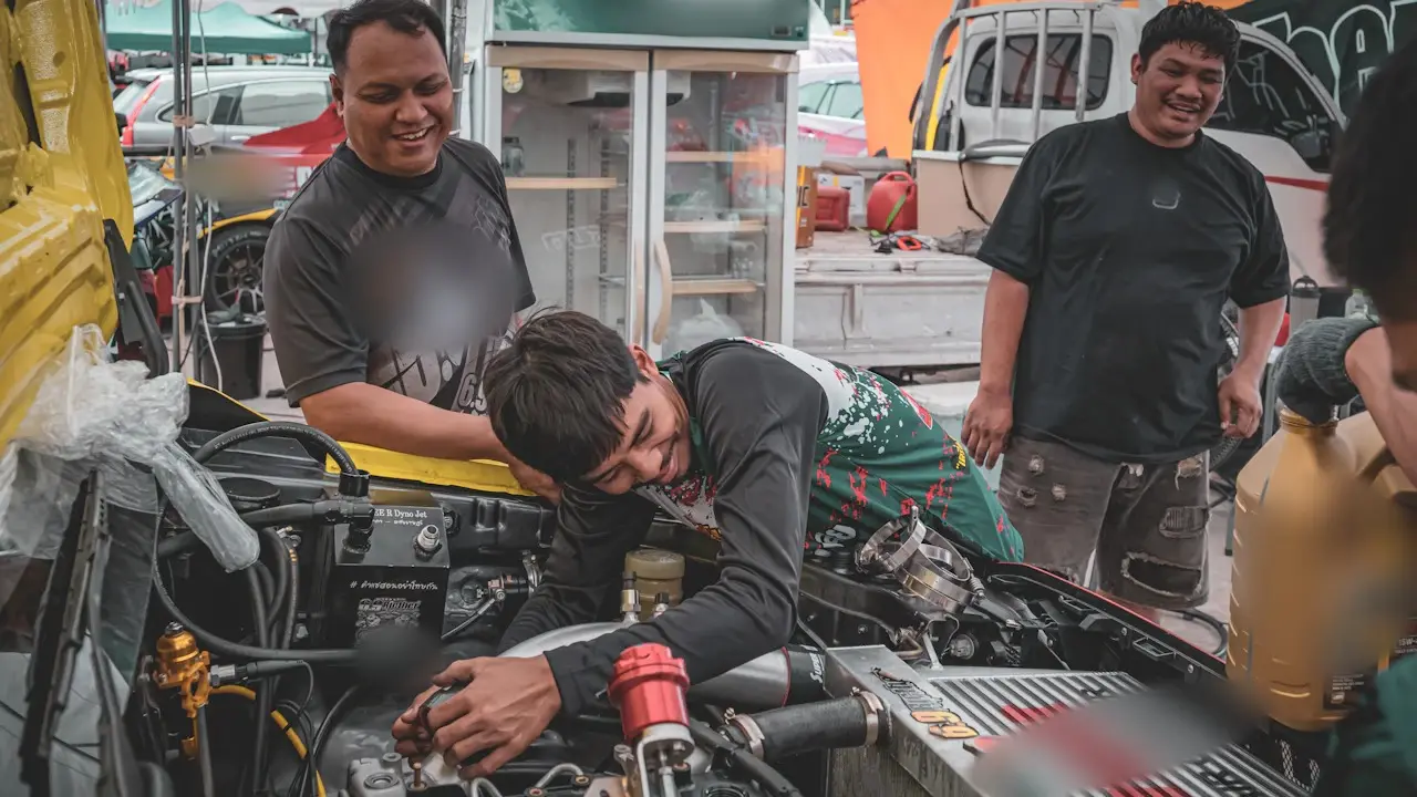 Three mechanics working on an open engine bay beside a bottle of motor oil.