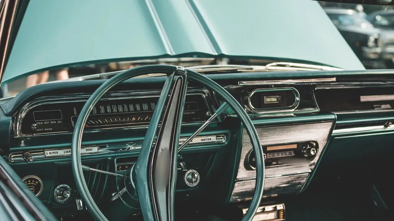 The dashboard and steering wheel of a 1960s American sedan, with its hood raised.