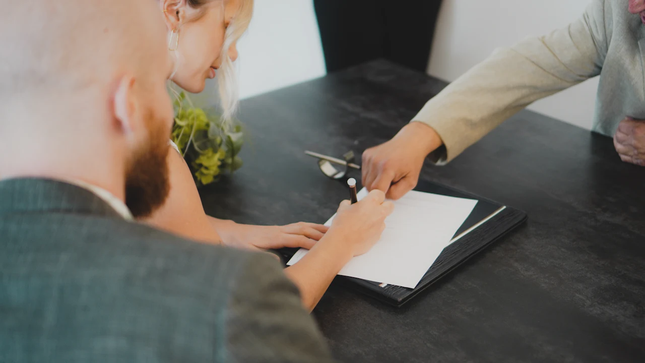 A person signing car sale paperwork at a desk with a pen