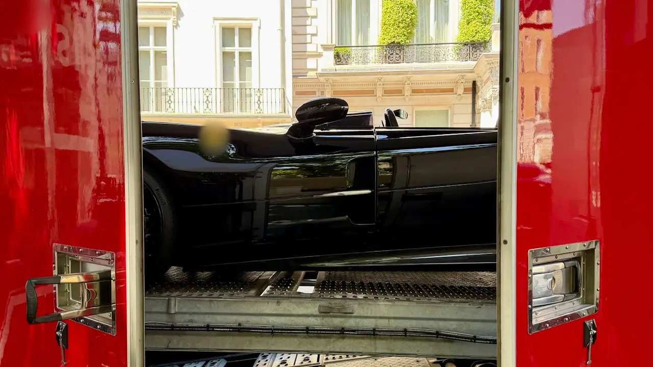 A sports car on the deck of an enclosed car transporter, seen between its open doors.