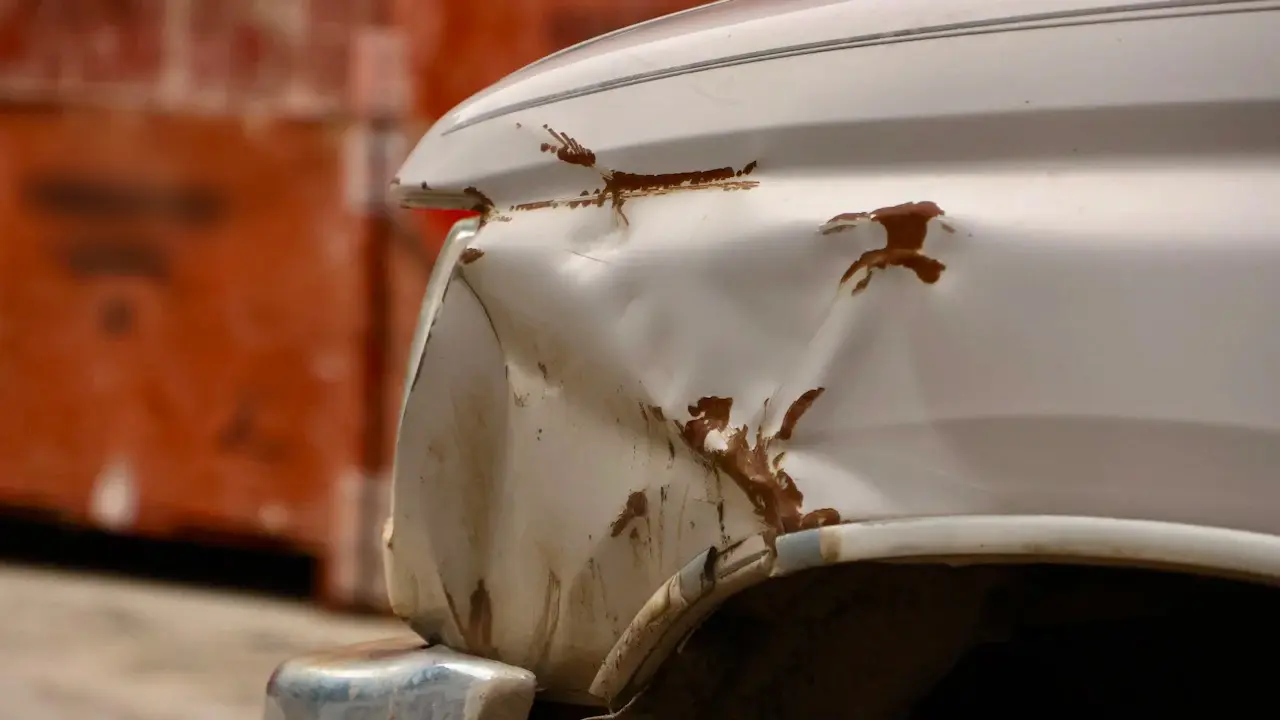 A dented, rust-marked white car fender above the wheel arch.