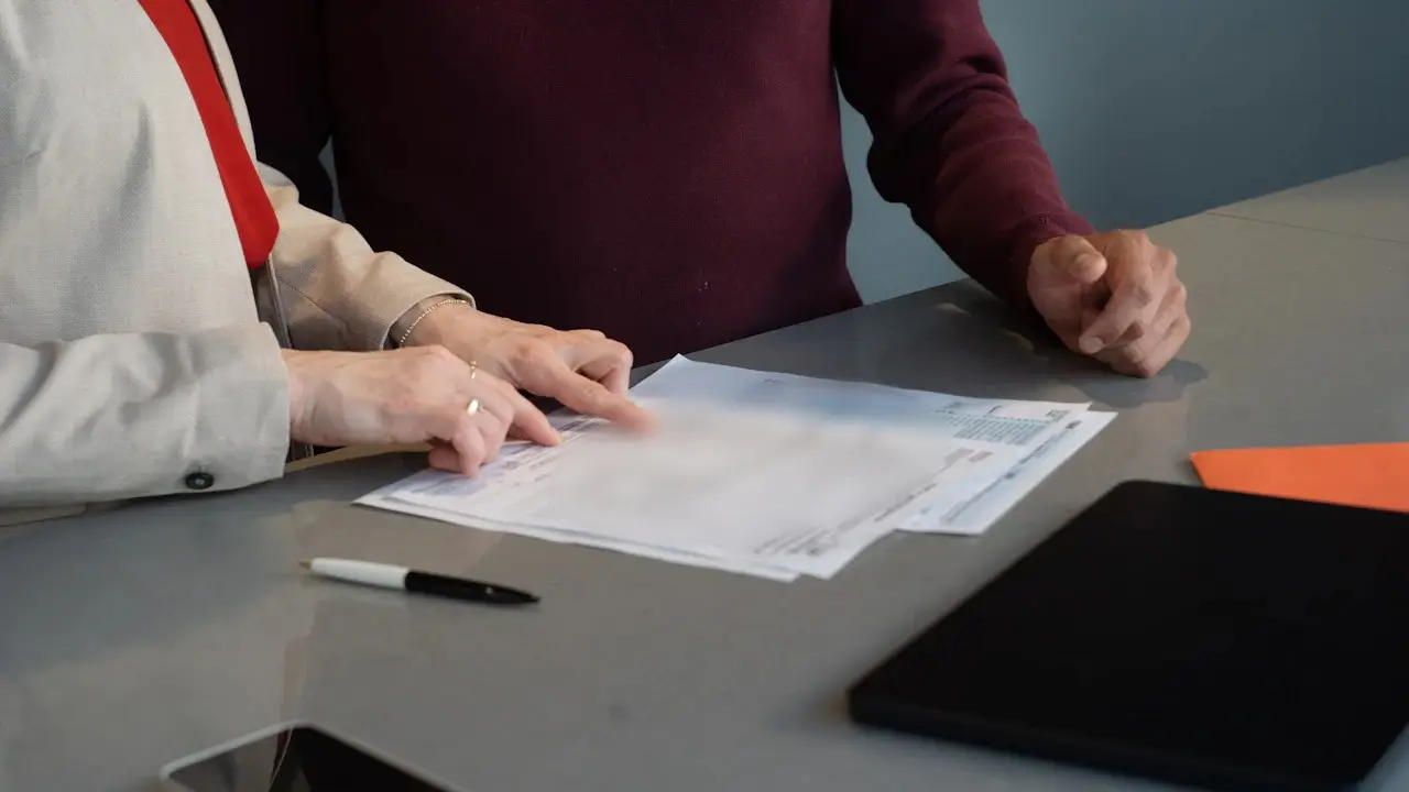 Two people going over a printed form on a desk, with a pen beside it.
