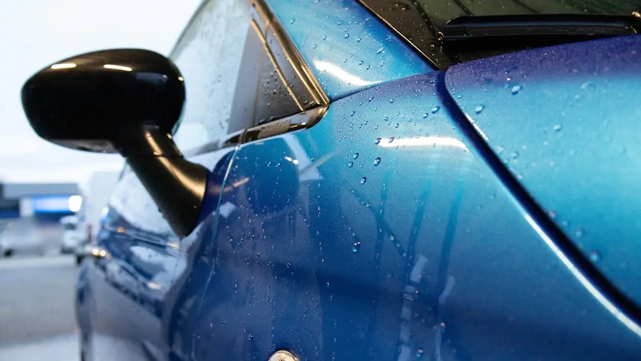 Close view of a wet blue car door panel and its side mirror.