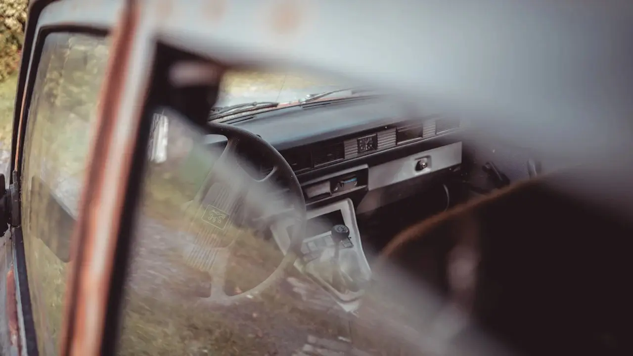 The rusted door frame and worn interior of an old car, seen through the open driver’s door.