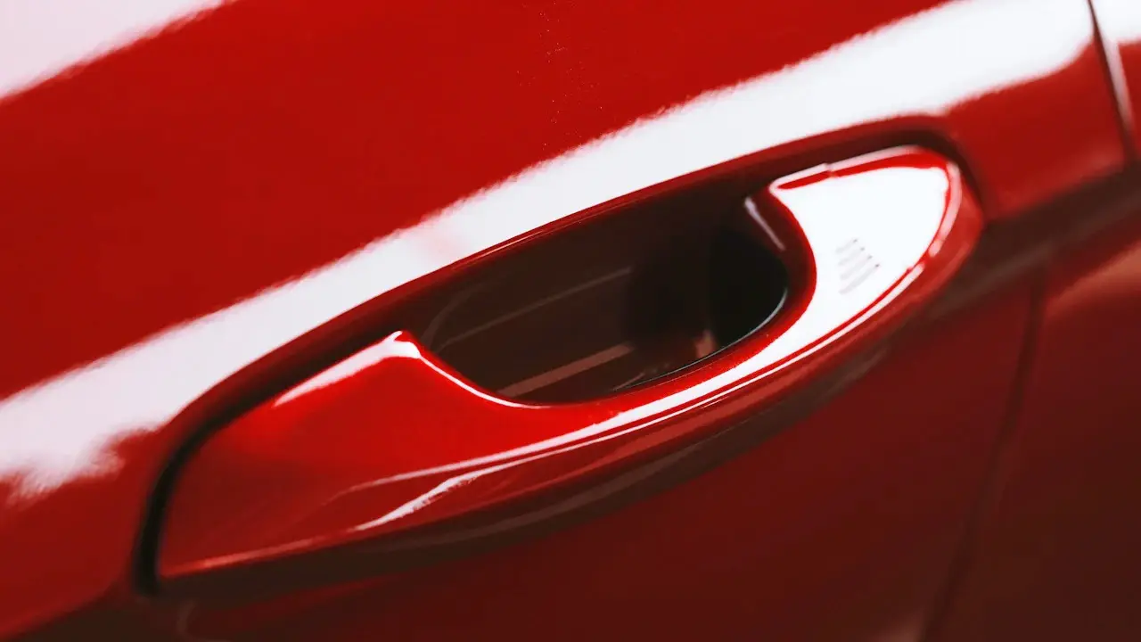 Close view of a red car's door handle and the paint around it.