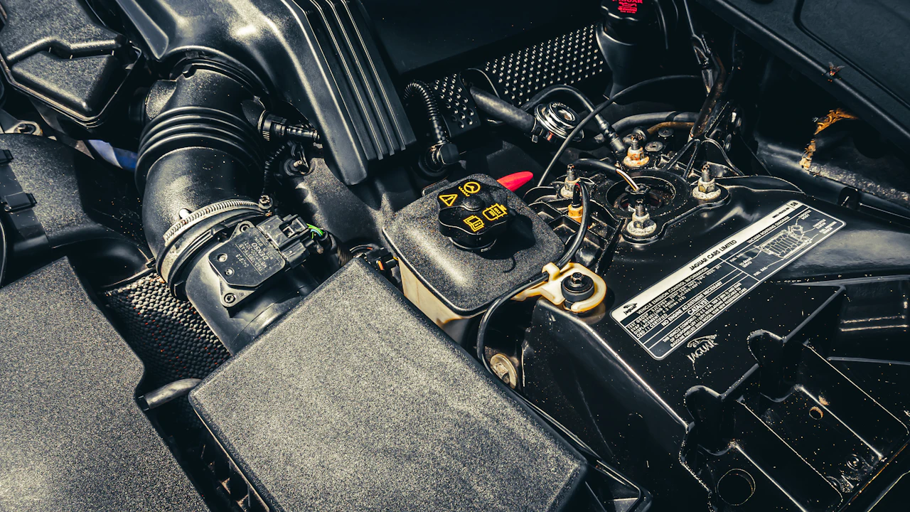 A close view down into an engine bay, the air intake ducting, coolant reservoir, battery terminals and a printed specification plate all visible