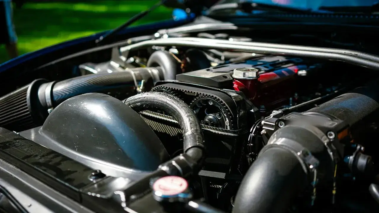A tuned engine bay under an open hood: the radiator cap, a braided coolant hose, the timing-belt pulleys, a large intake and the throttle body.