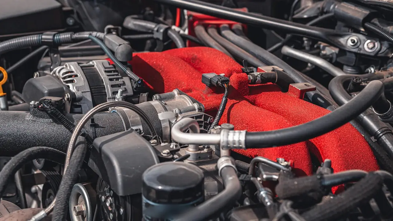 A modern engine bay with a red intake manifold, the dipstick handle at the edge and the oil filter in front.