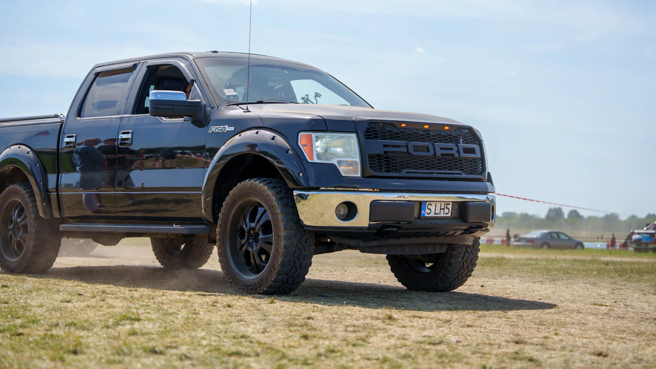 A black American crew-cab pickup on dry grass at a European show field, foreign plate on the bumper