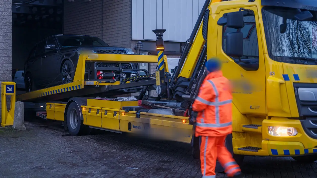 A dark SUV being loaded onto a yellow flatbed tow truck, with an operator beside it.