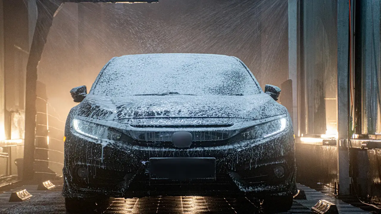 A hatchback covered in wash foam in a wash bay.