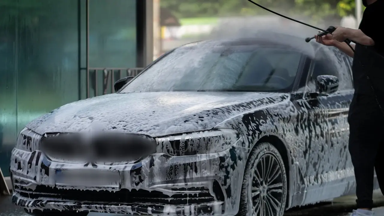 A foam-covered sedan being rinsed at a car wash.
