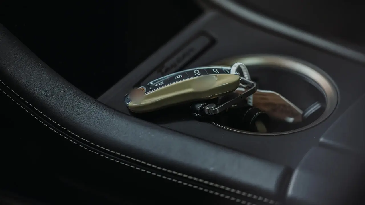 A car's key fob resting in a centre-console cupholder; the fob's crest and logo blurred.