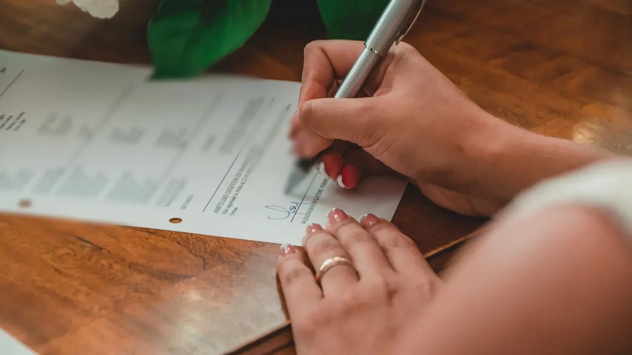 A hand signing a printed form with a pen.