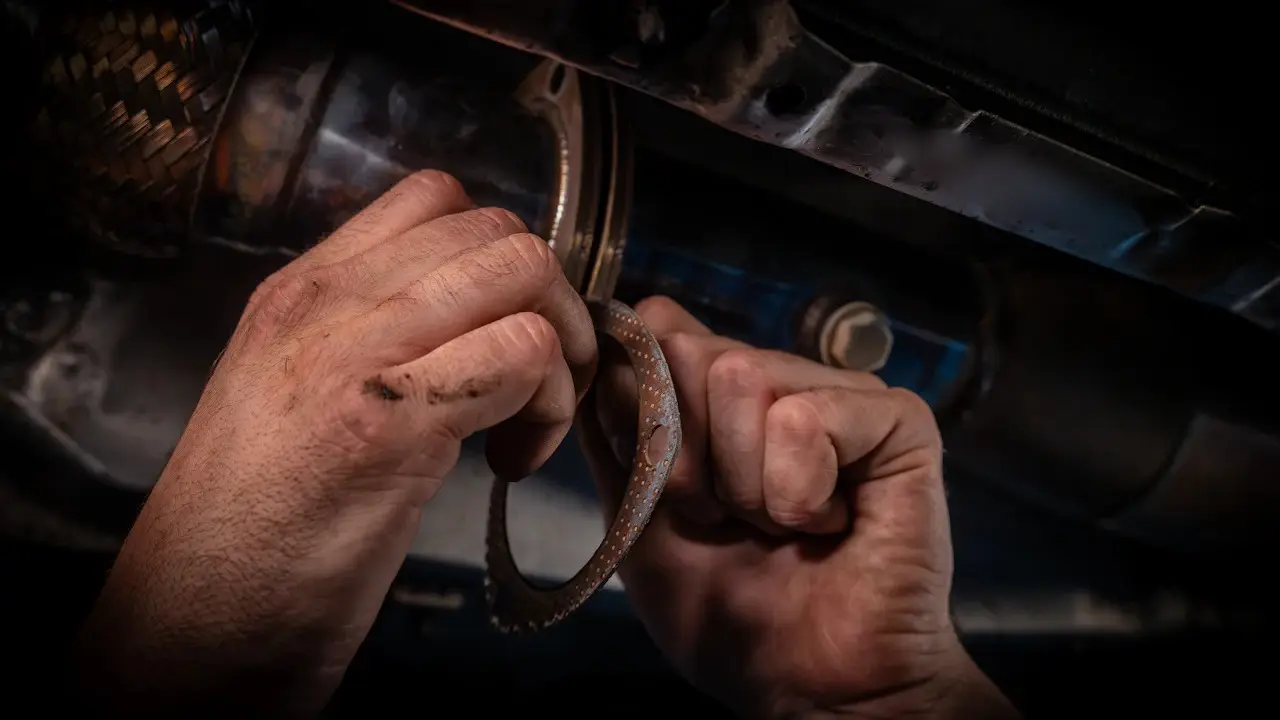 Hands fitting an exhaust gasket to a pipe flange beneath a car.