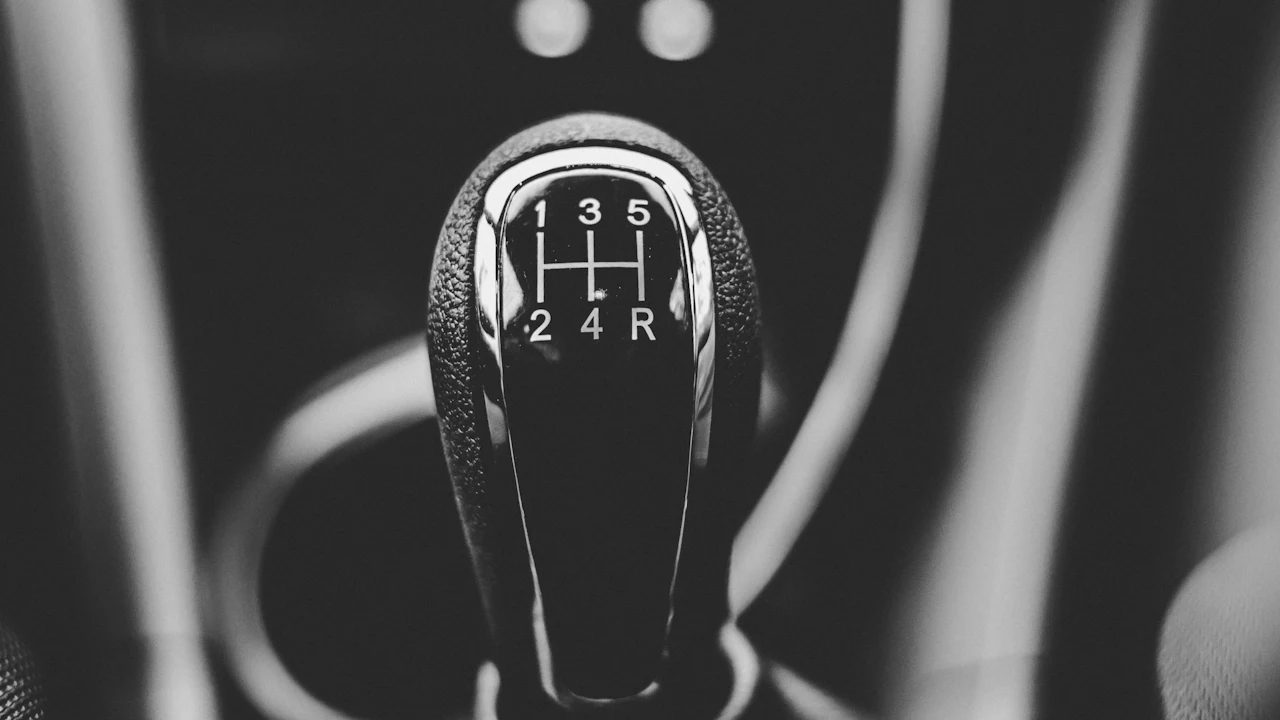 A manual gear knob photographed close up in black and white, the shift pattern visible on top
