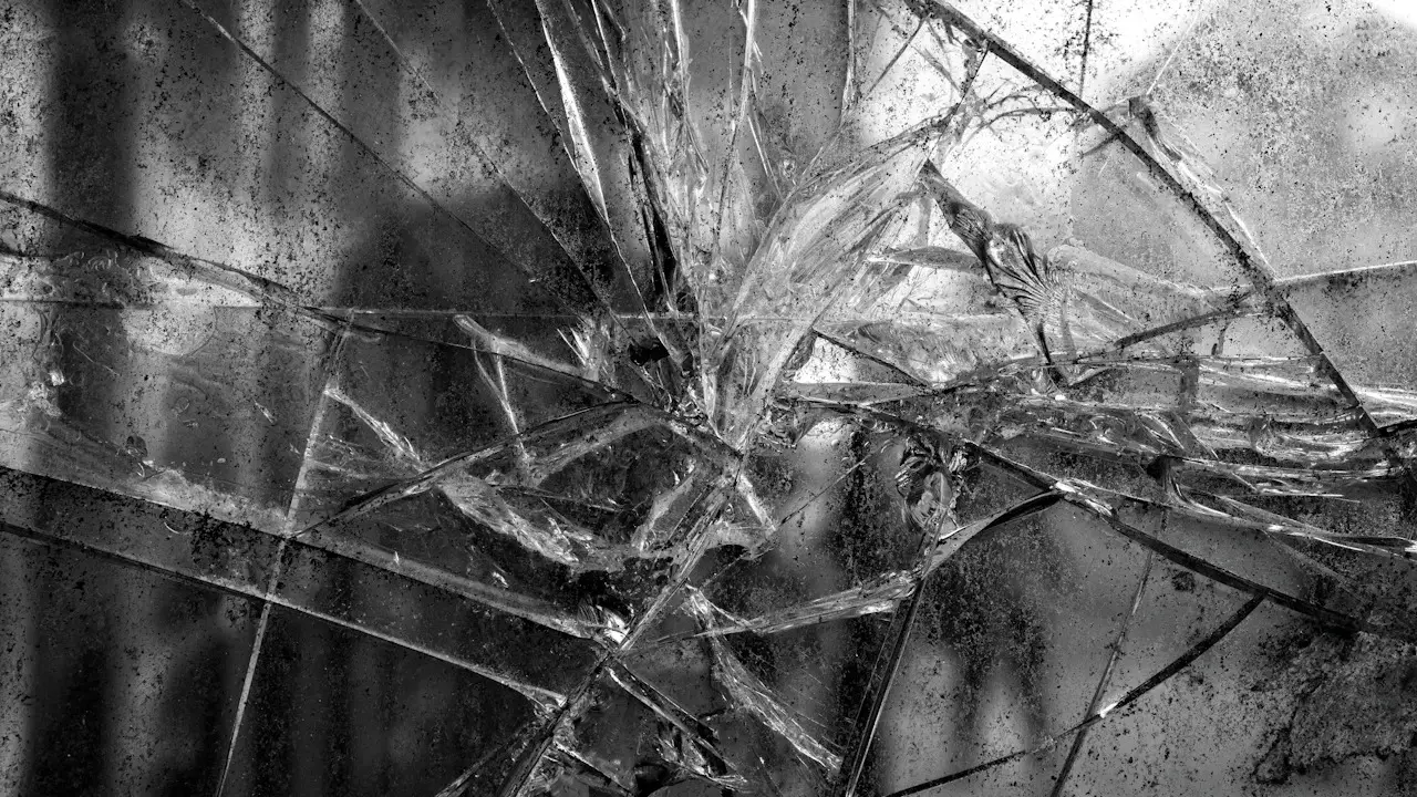 Black-and-white close view of shattered glass radiating from an impact point.