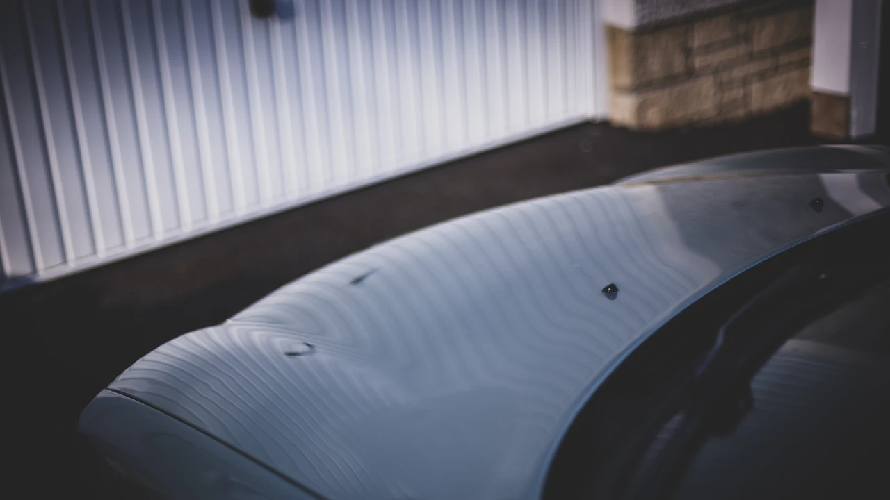A close-up of a car roof panel in low sunlight showing a scatter of small shallow dents