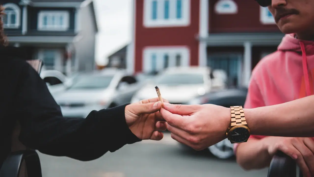 One person handing a car key to another in front of parked cars and houses.