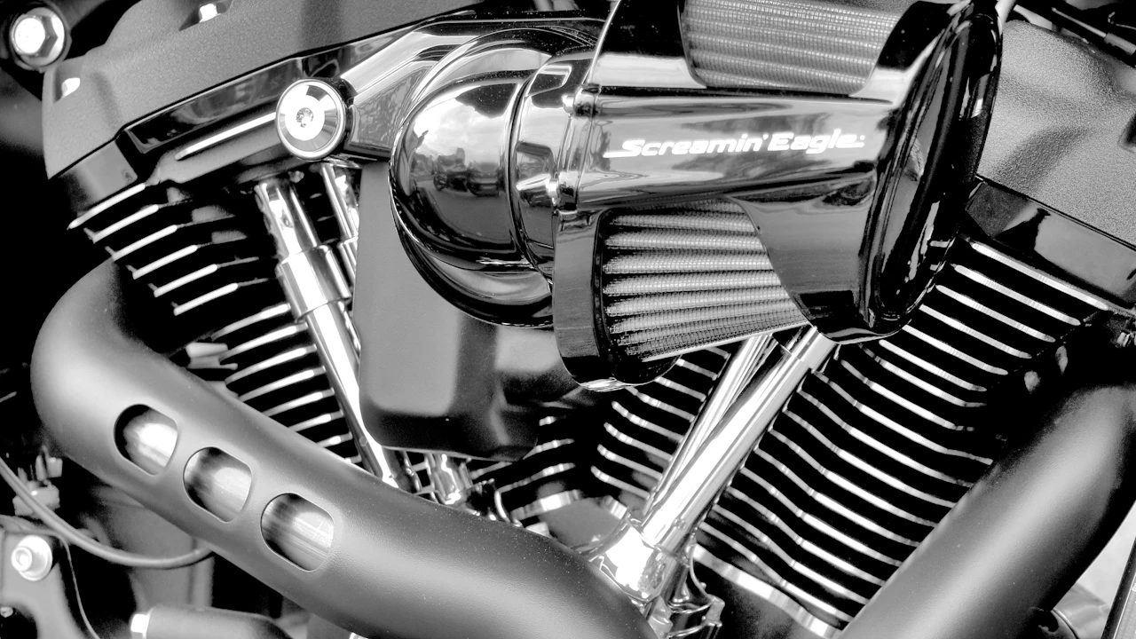A Harley-Davidson V-twin engine in close-up, chrome pushrod tubes and cooling fins filling the frame around a branded intake